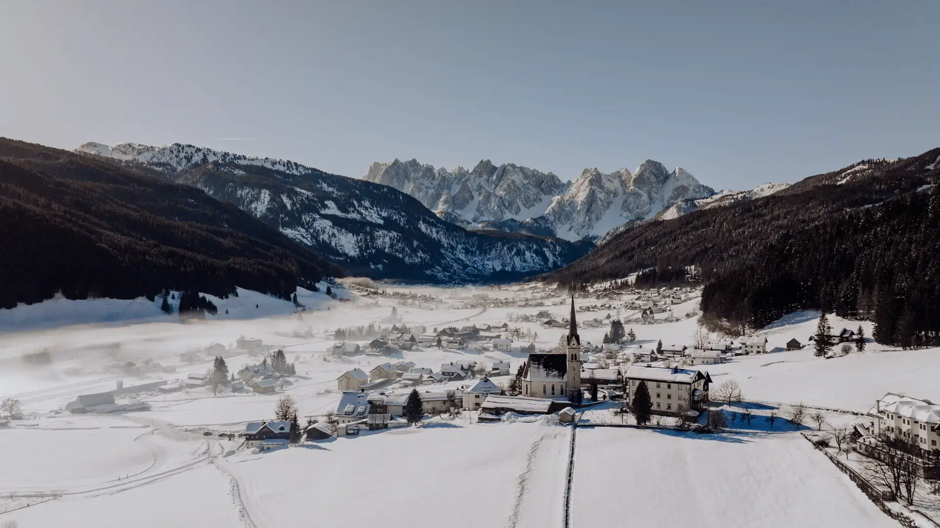 Luftaufnahme von Gosau im Winter mit Kirche und Blick auf den Gosaukamm.