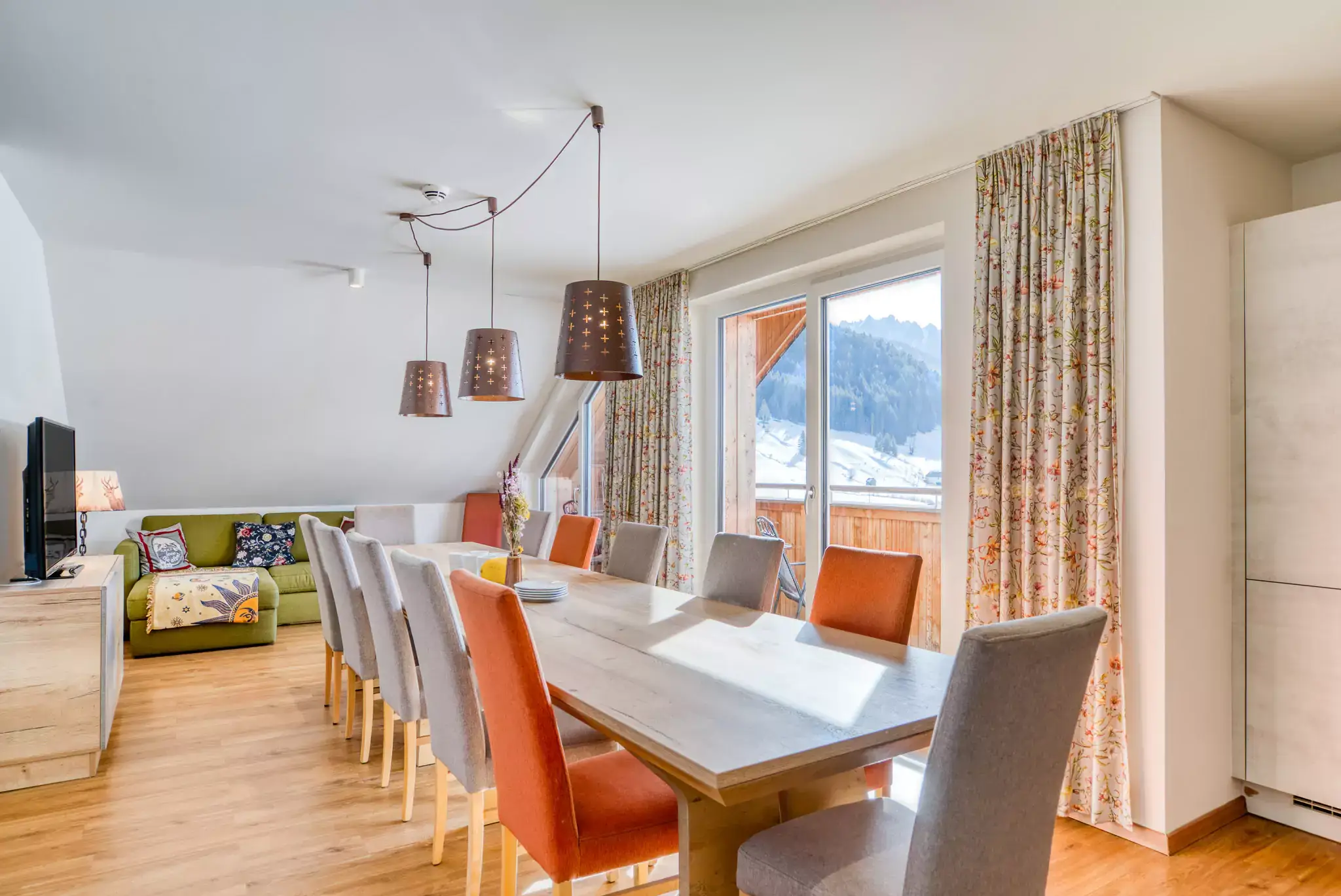 Das Wohnzimmer mit Tisch,TV und Balkon im Gigantos Apartment im COOEE alpin Hotel Dachstein in Gosau.