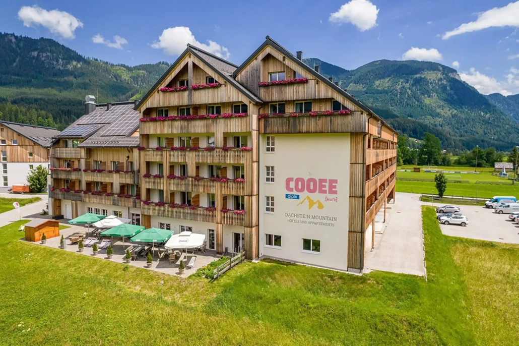 Das COOEE alpin Hotel Dachstein von außen im Sommer mit Sonnenterrasse.