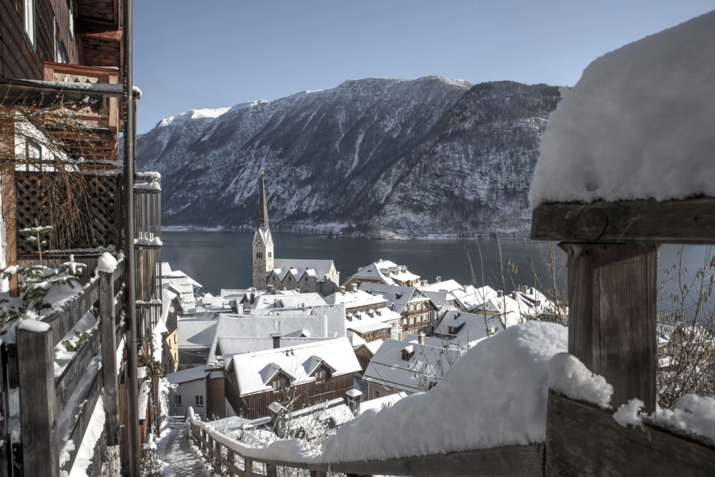 Blick auf Hallstatt im Schnee mit der Kirche im Fokus und dem Hallstätter See und verschneiten Bergen im Hintergrund.