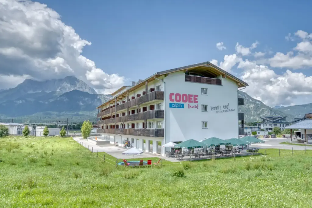 Das COOEE alpin Hotel Kitzbüheler Alpen von außen im Sommer mit einer Sonnenterrasse.