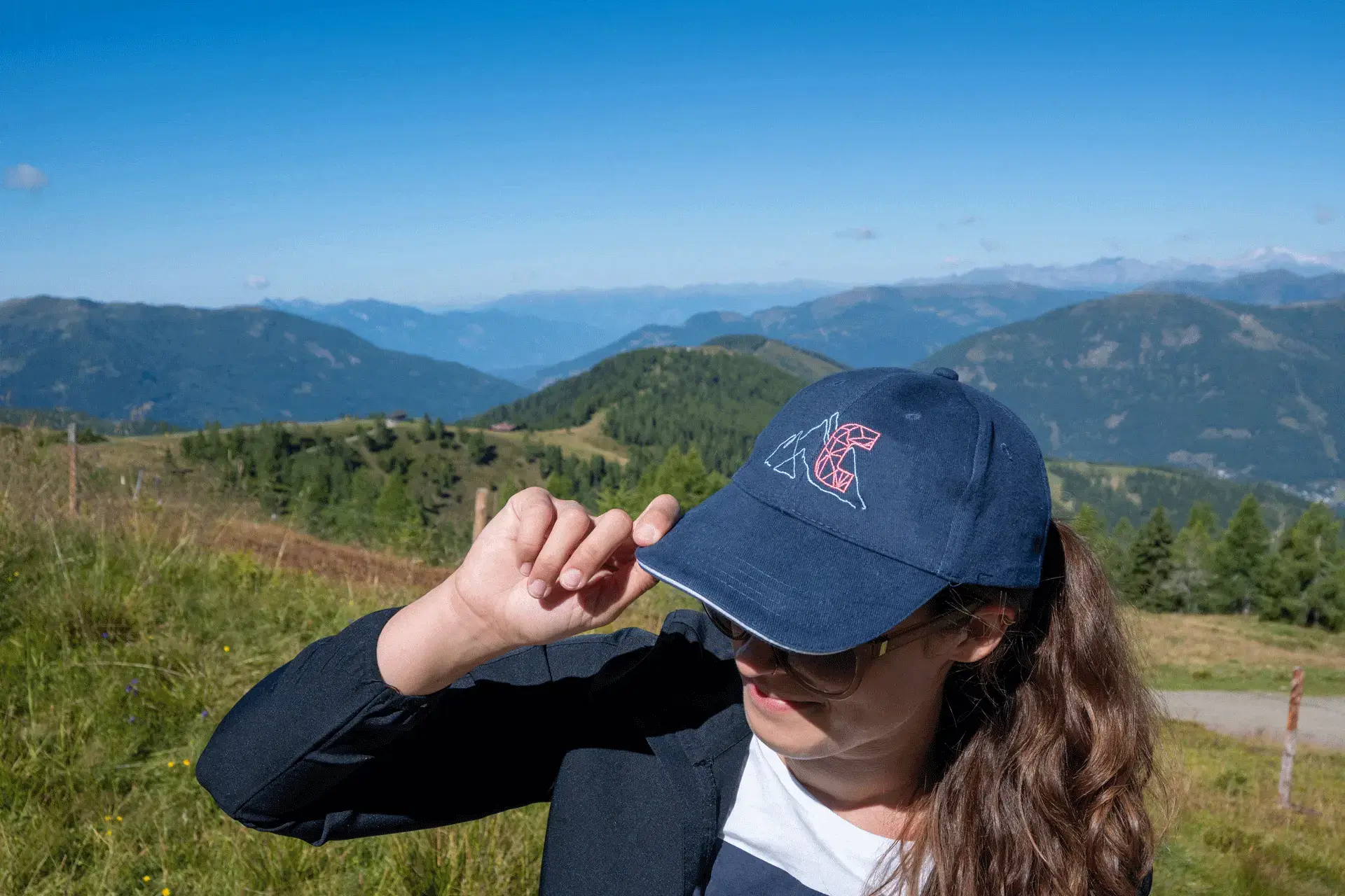Frau trägt die dunkelblaue COOEE alpin Cap „Alinga“ beim Wandern in den Alpen – stylische Outdoor Kappe für Sonnenschutz, Wanderurlaub und Abenteuer in Österreich.