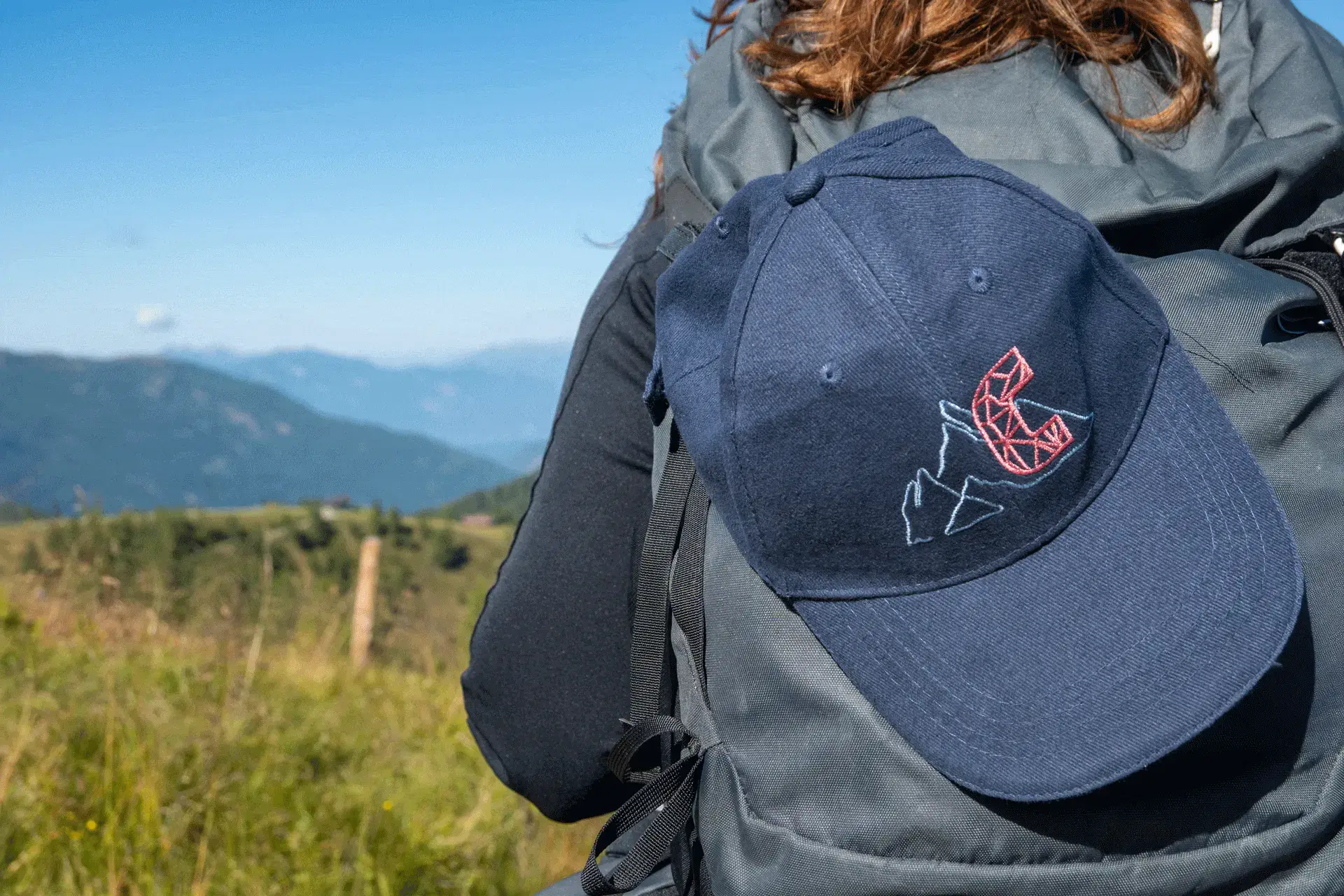 Dunkelblaue COOEE alpin Cap „Alinga“ auf einem Wanderrucksack in den Alpen – stylische Wanderkappe für Outdoor-Abenteuer, Sonnenschutz und Freizeit in Österreich.