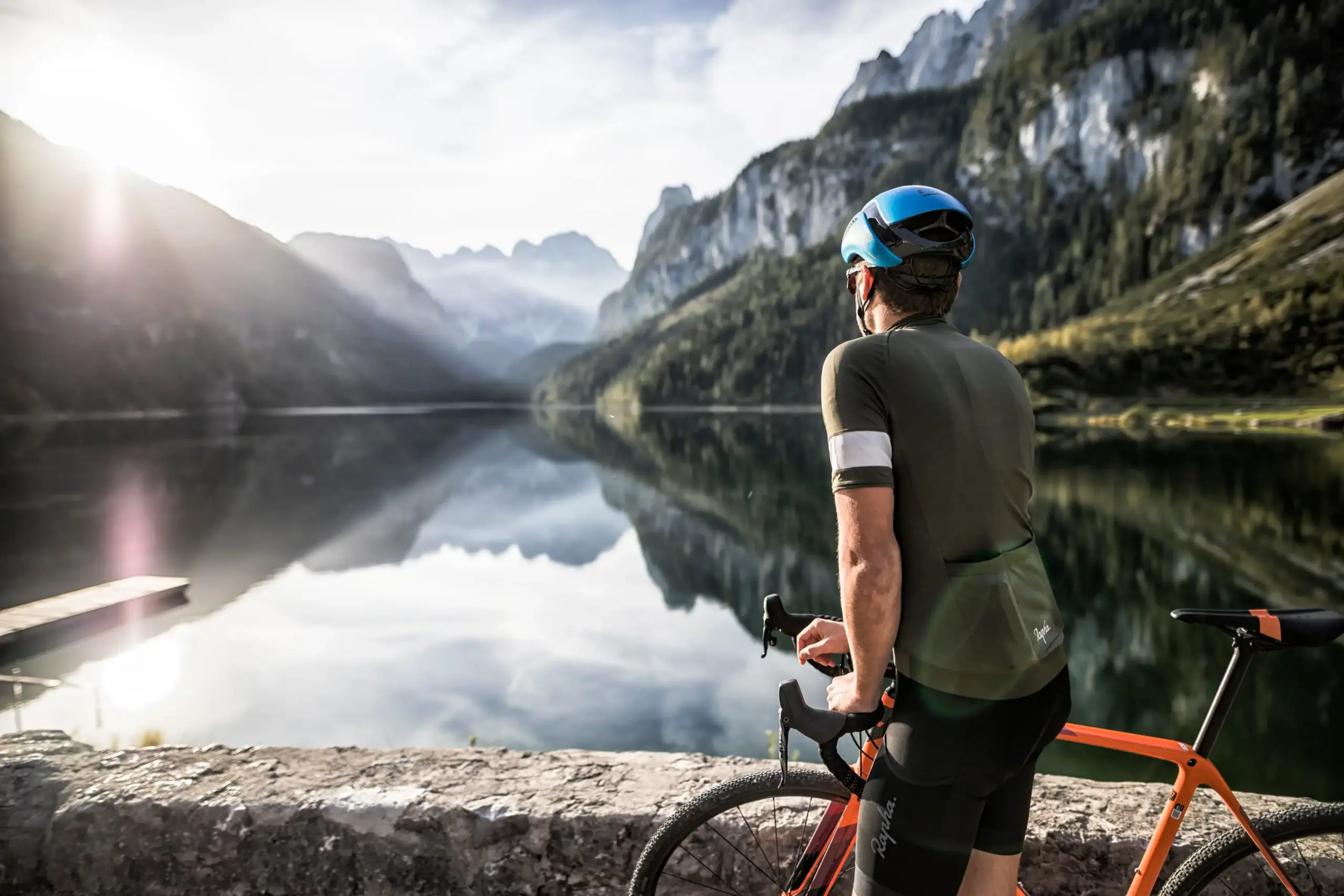 Mountainbiker s kolem u jezera Gosausee v Salzkammergut s výhledem na masiv Dachstein a odraz hor v jezeře.