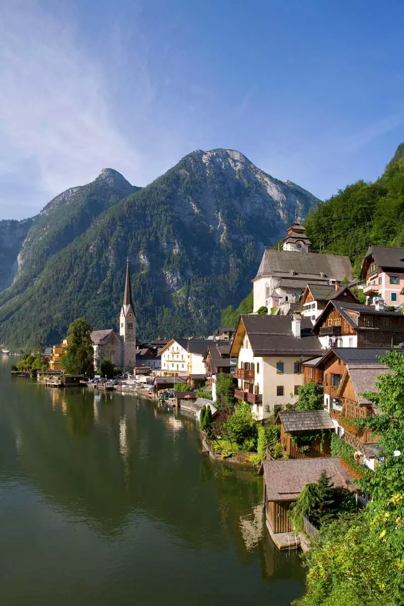 Hallstatt mit seinen charakteristischen Häusern und der Kirche am Hallstätter See im Sommer mit einem Bergpanorama im Hintergrund.