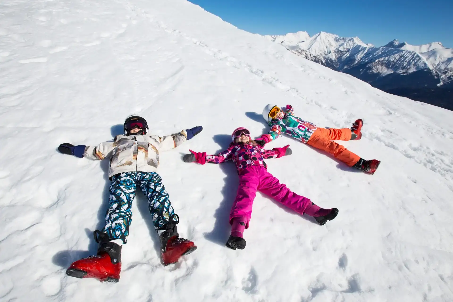 Drei Kinder in bunter Skibekleidung machen Schneeengel im Skigebiet Bad Kleinkirchheim – Kids on Ski Aktion für 3- bis 5-Jährige mit gratis Skikurs und Ausrüstung in Österreich.