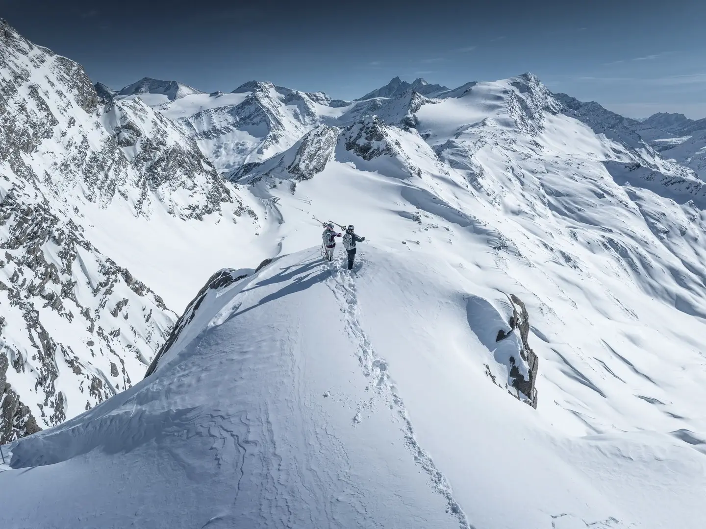 Twee freeriders, met hun ski’s op de schouder, genieten van het bergpanorama op de Kitzsteinhorn. Overal om hen heen besneeuwde bergtoppen.