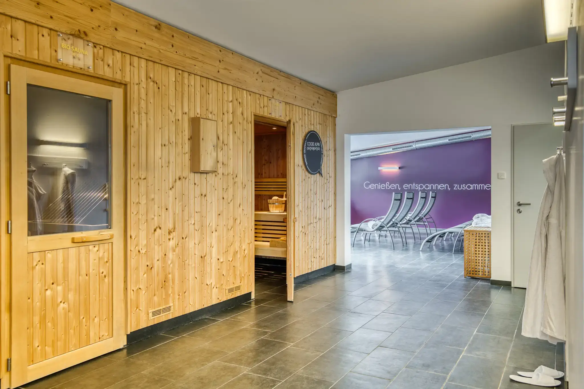 Zwei Saunen und ein Ruheraum. Rechts hängt ein Bademantel an der Wand.