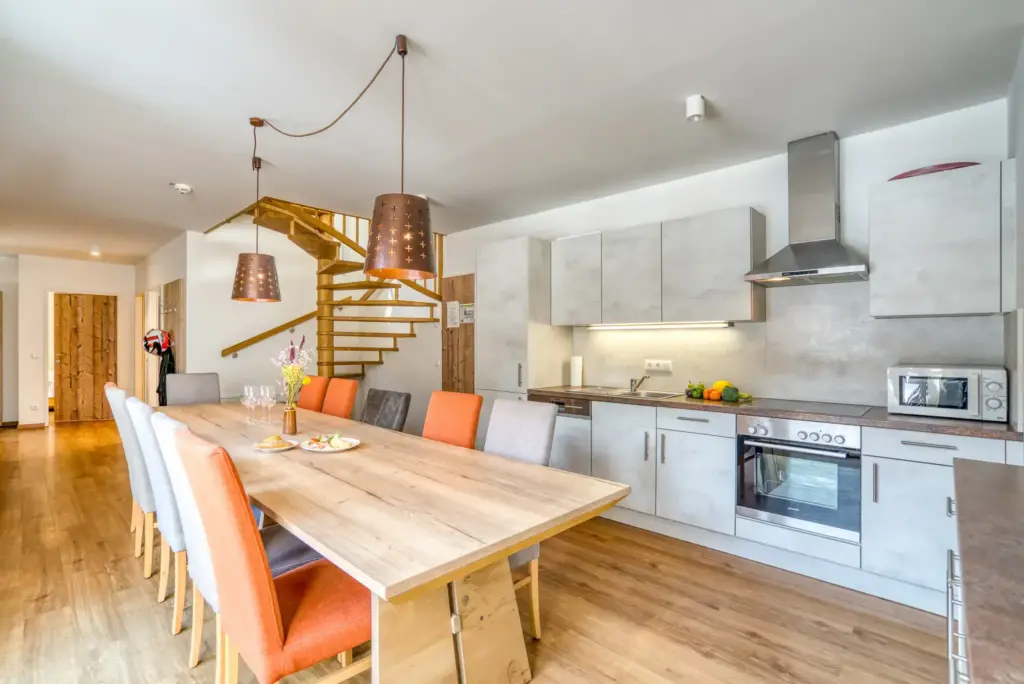 Modernes, großzügiges Apartment im COOEE alpin Hotel Gosau mit voll ausgestatteter Küche, großem Esstisch, gemütlichen Sitzmöglichkeiten und Holztreppe ins Obergeschoss – ideal für Familienurlaub oder Gruppenurlaub in den Bergen nahe dem Skigebiet Dachstein West.