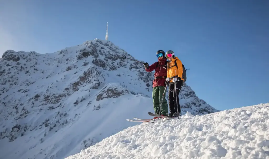 Zwei Skifahrer:innen genießen die Aussicht am verschneiten Kitzbüheler Horn in St. Johann in Tirol – perfekter Startpunkt für Skiurlaub in den Kitzbüheler Alpen mit Pisten, Wintersonne und alpiner Bergwelt.