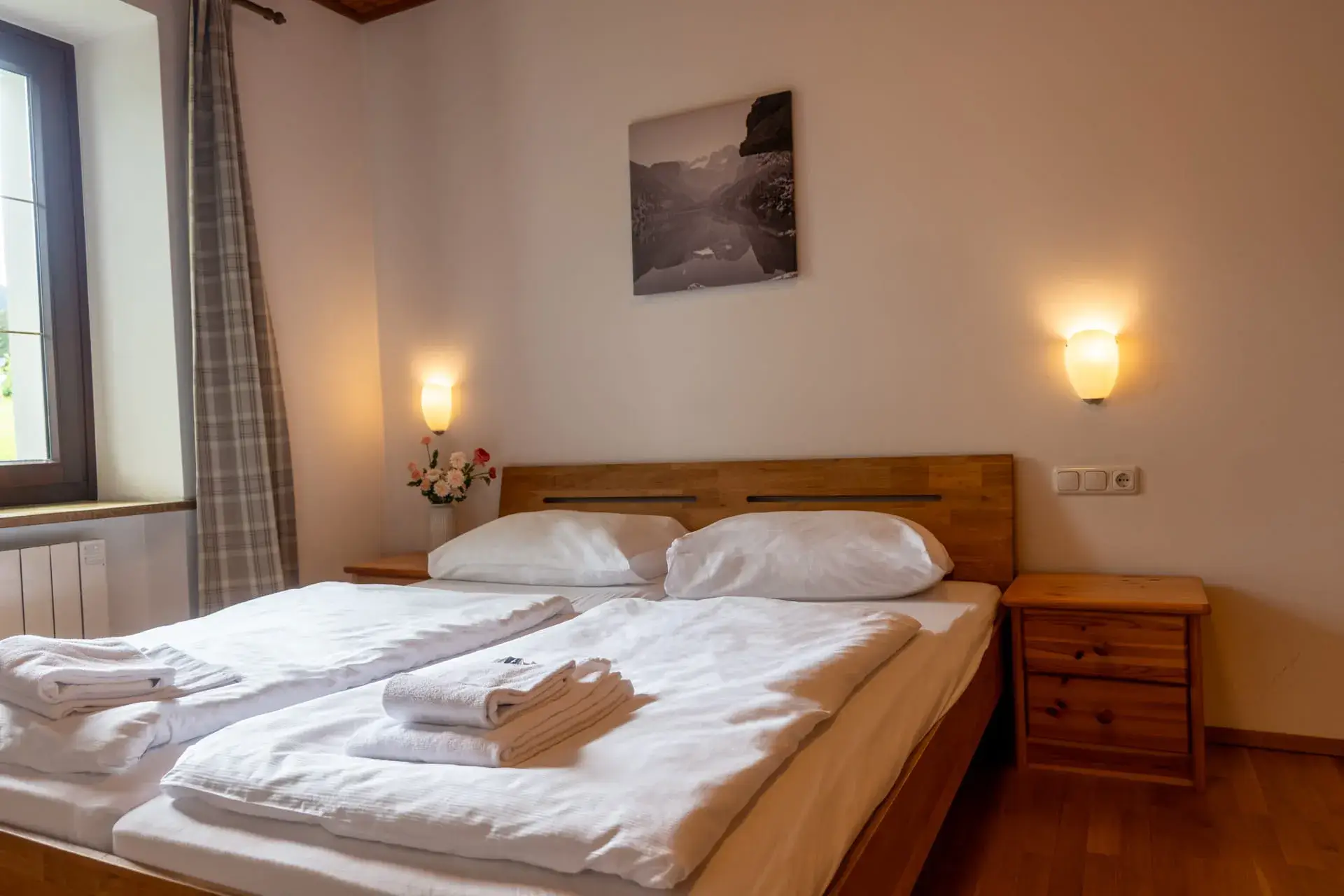 Útulná ložnice v apartmánu u jezera Traunsee v Ulmenhofu s manželskou postelí, nočními stolky a dřevěným nábytkem v regionálním stylu.