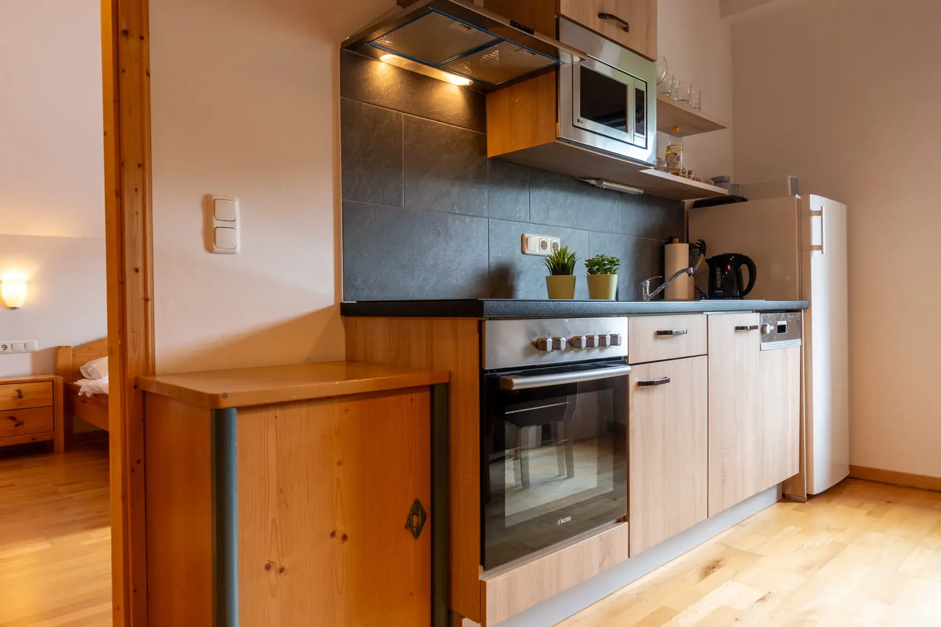 cucina moderna con piano cottura in vetroceramica, forno e microonde, vari utensili da cucina riposti su una mensola a muro, frigorifero grande e capiente