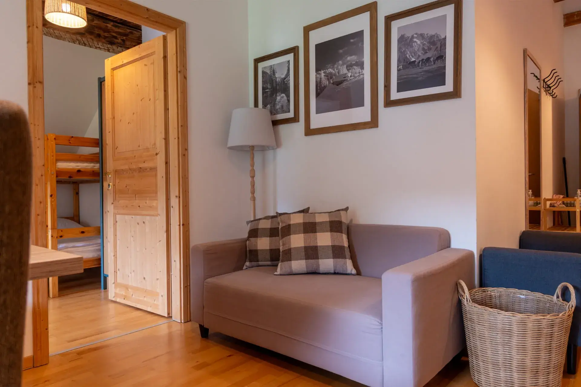 divano grigio con cuscini decorativi, lampada da terra e cesto della biancheria; sopra il divano, quadri raffiguranti paesaggi della regione