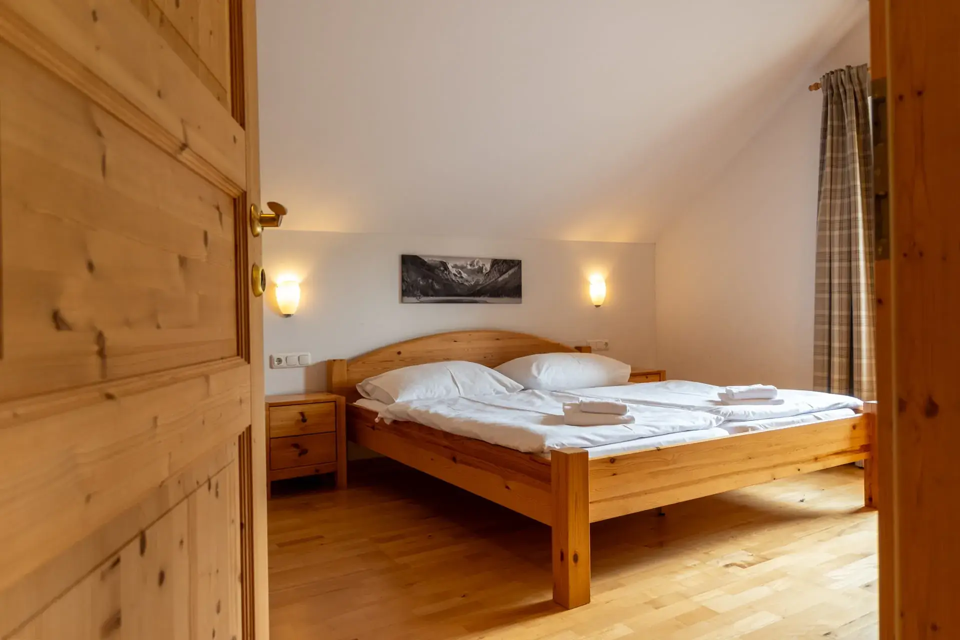 un comodo letto matrimoniale con due comodini, un quadro panoramico sopra il letto, una finestra con tende lunghe