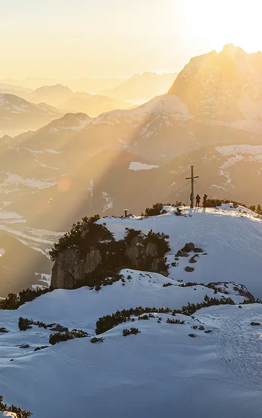 Verschneiter Berggipfel mit Gipfelkreuz im warmen Abendlicht im Pillerseetal.